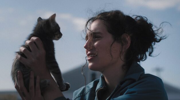 A woman holds a cat while standing outside.
