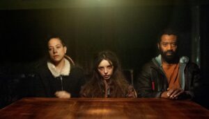 Two women and one man sit in front of a table in an oddly lit room.